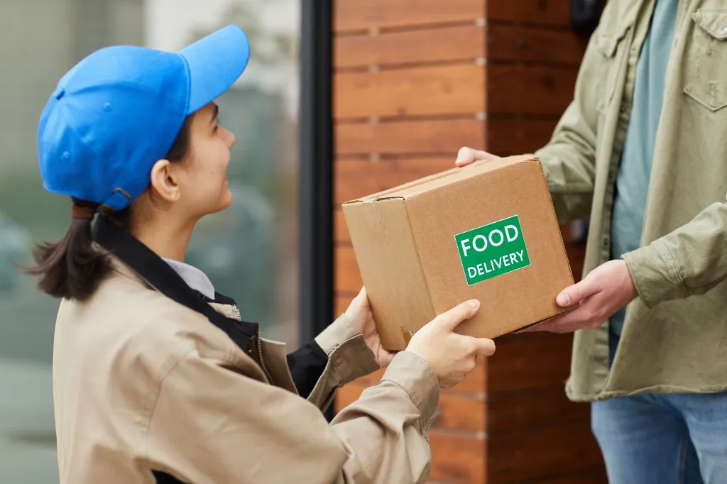 young-courier-giving-cardboard-box-man-while-they-standing-outdoors-she-delivering-food.webp